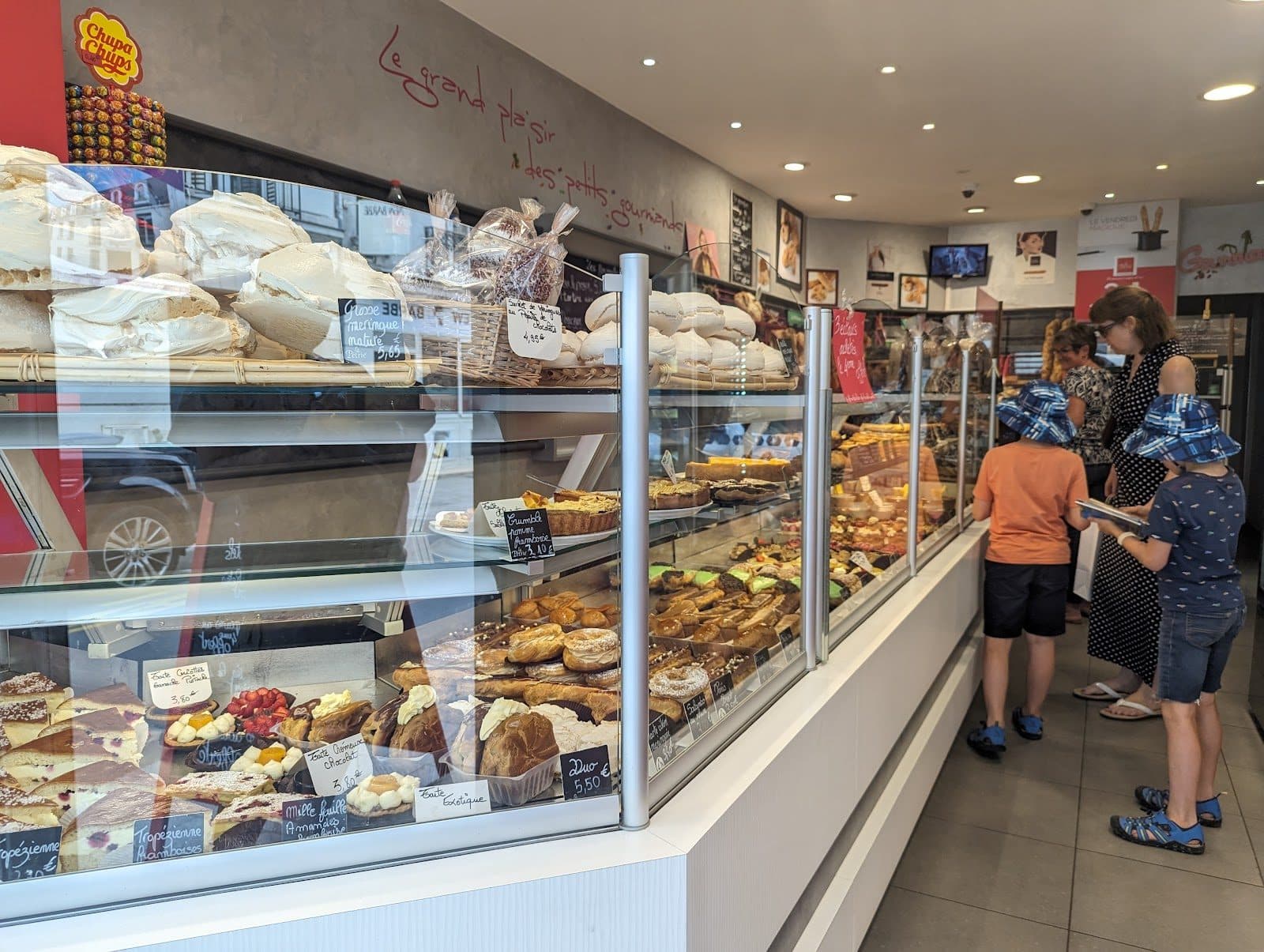 La longue vitrine de la boutique vue depuis l’entrée, des clients au comptoir au fond.