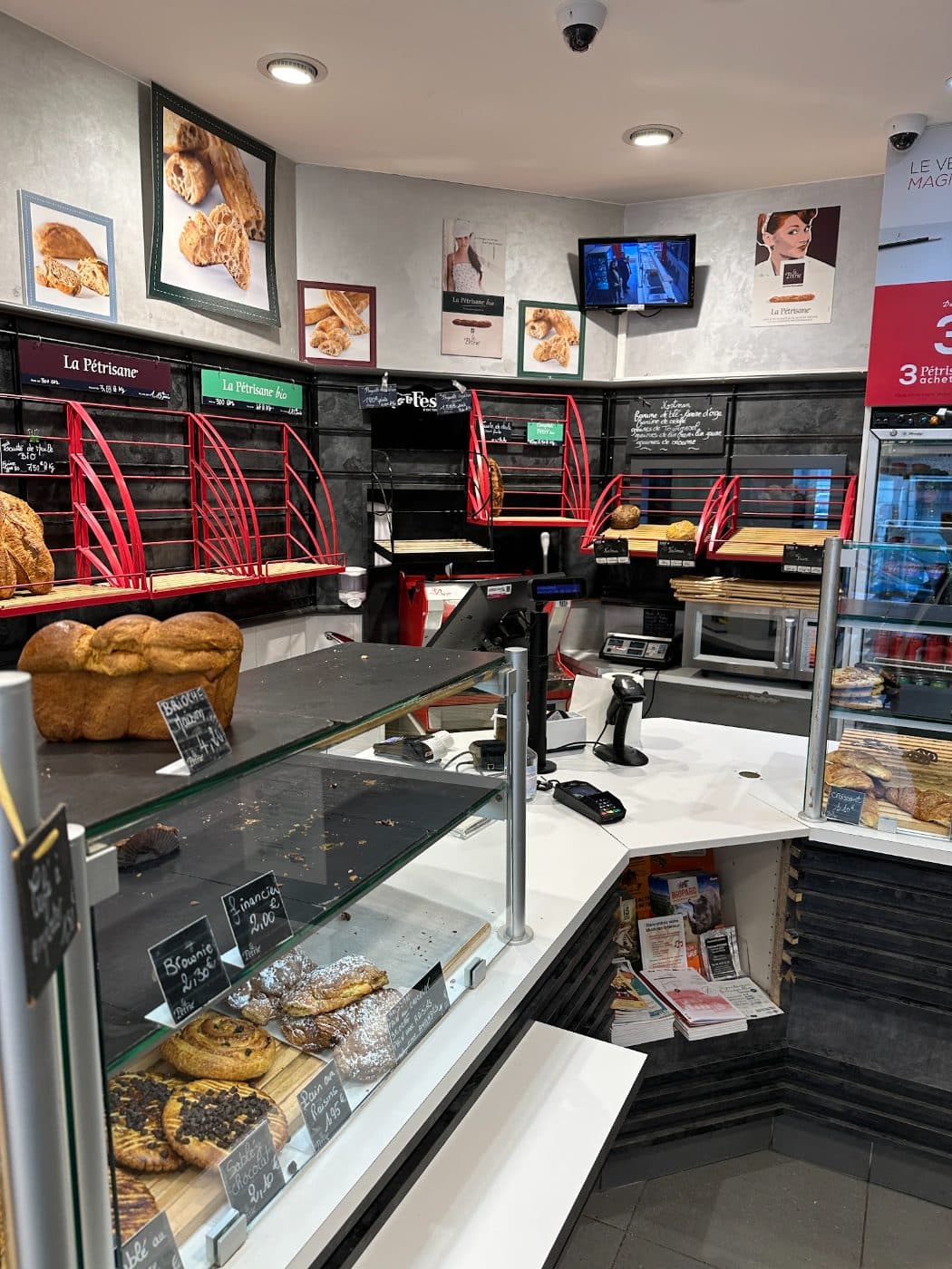 Le fond de la boutique, casiers à pain rouges, ardoises manuscrites et affiches au mur.