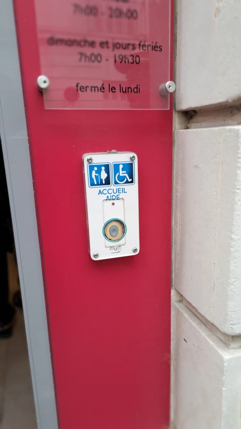 Le montant framboise de la devanture : la plaque d’horaires et le bouton d’appel « Accueil / Aide ».
