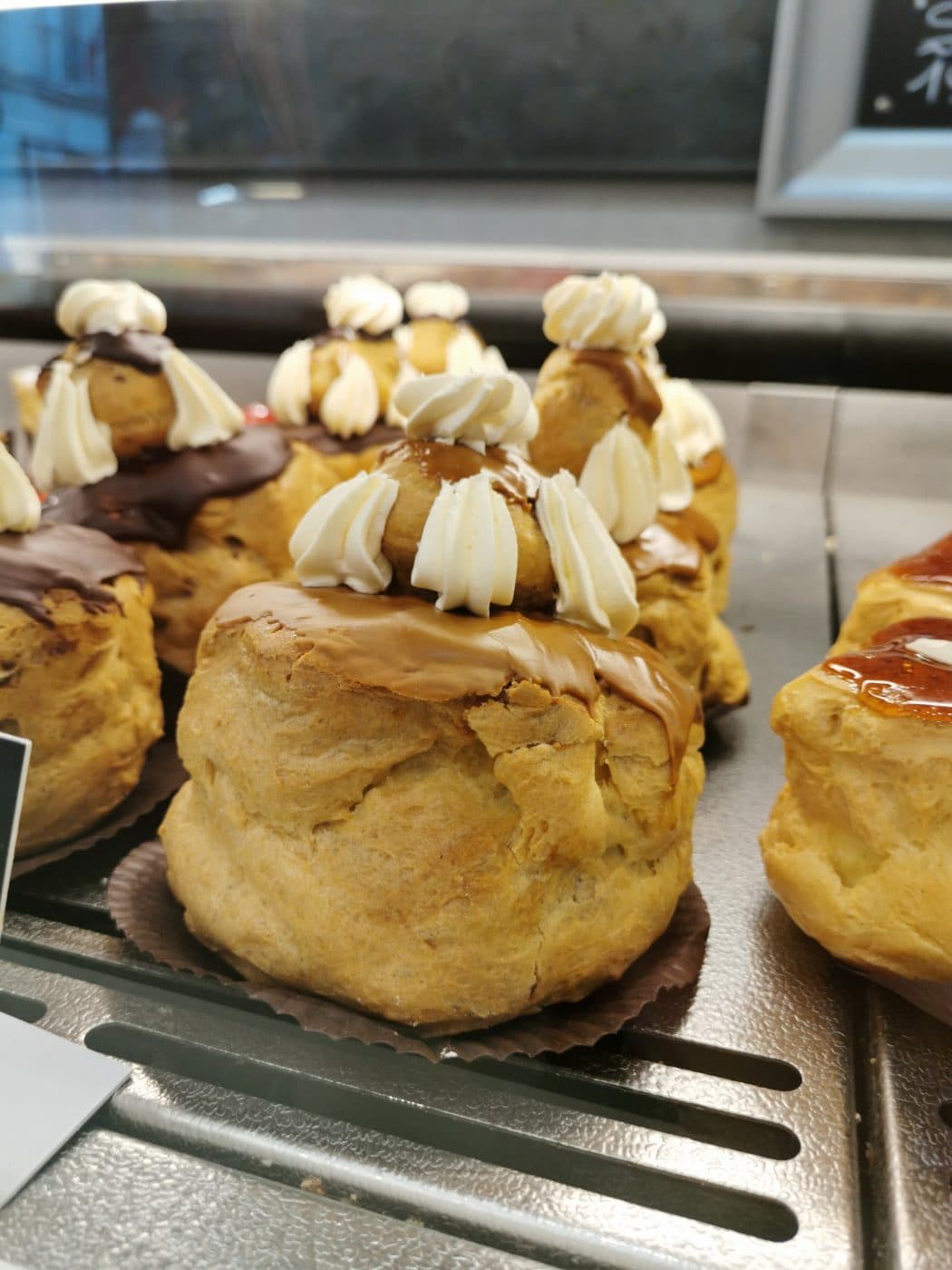 Gros plan sur des choux à la crème dans la vitrine, coiffés de crème montée et de caramel.