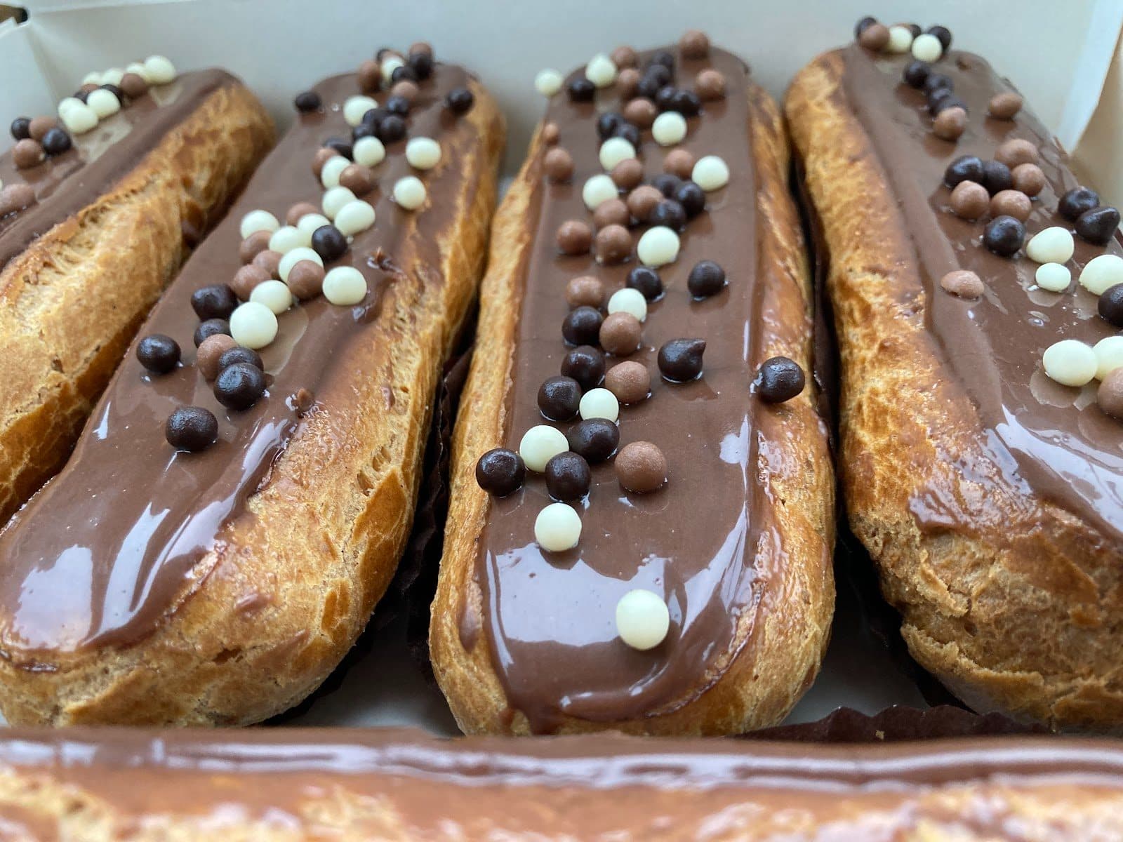 Des éclairs glacés au chocolat, alignés et parsemés de perles de chocolat blanc et de chocolat au lait.