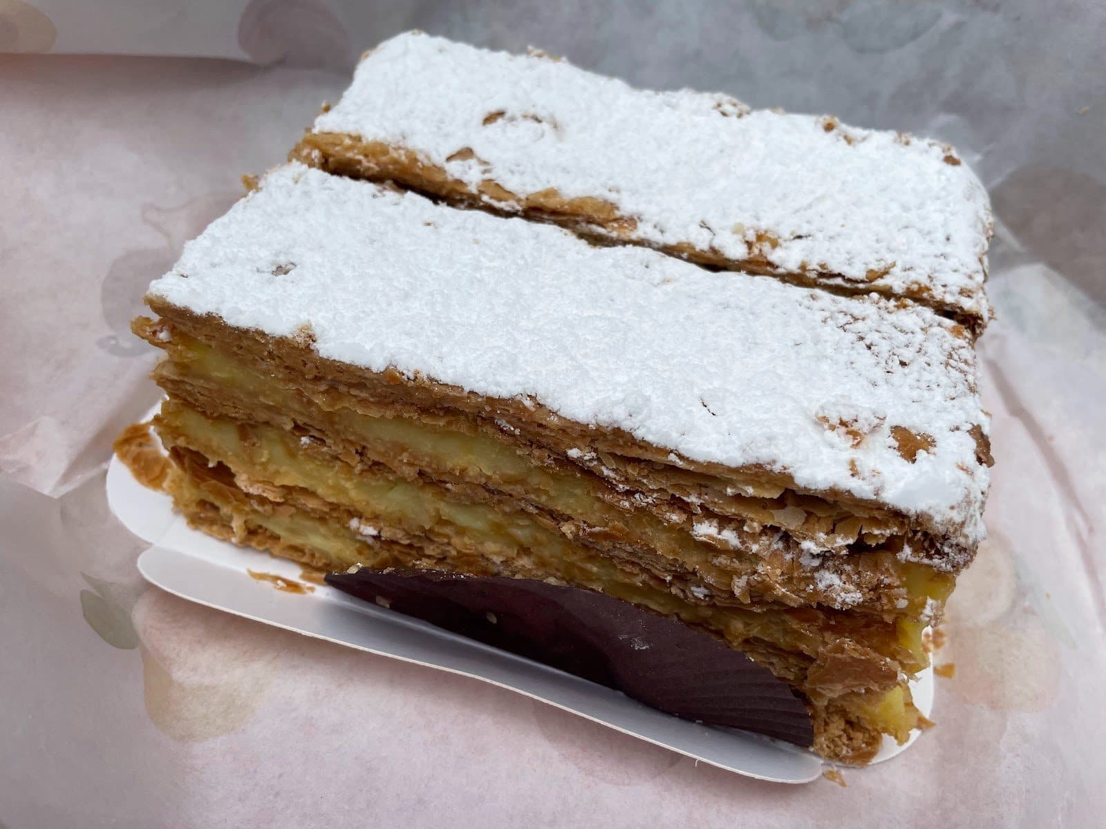 Une part de mille-feuille sur son papier, feuilletage caramélisé et sucre glace sur le dessus.